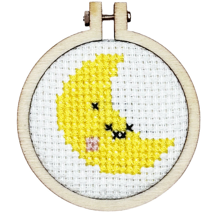 Cross-stitched yellow moon in a wooden hoop on a white background