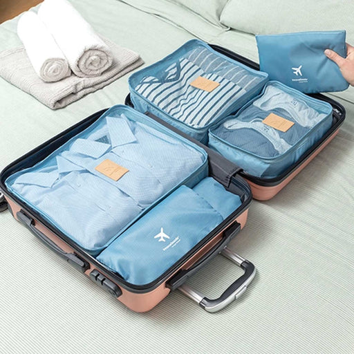 5 blue luggage organiser bags of various sizes containing  clothing, in an opening pink suticase on a bed 
