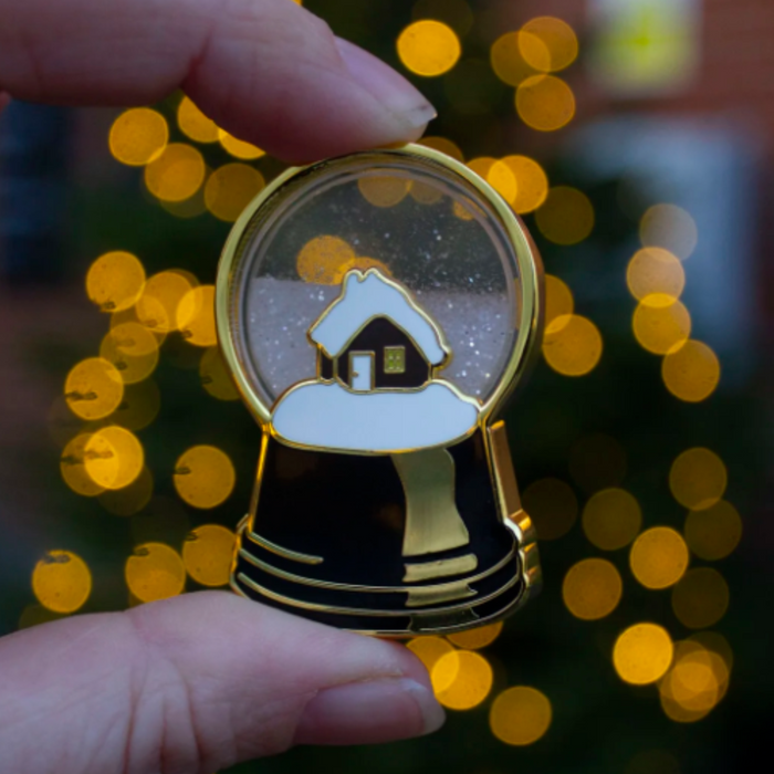 Small decorative item resembling a snow globe with a house inside, held by a hand against a blurred bokeh background.