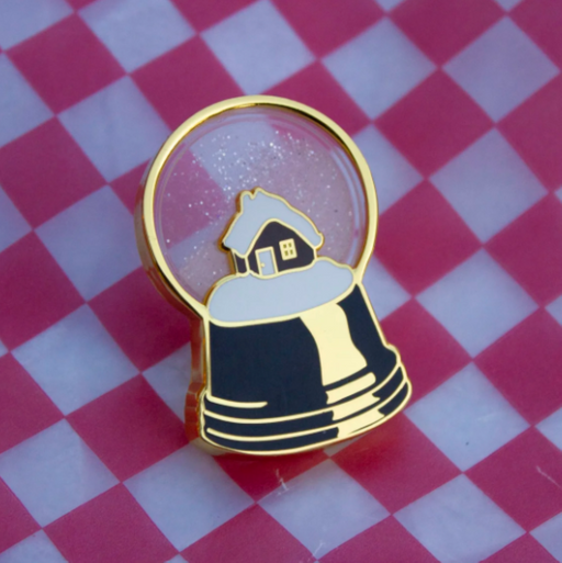Pin with a design of a house inside a snow globe on a red and white checkered background