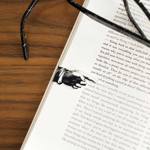 open book with text on page and black and white pointing finger shaped bookmark