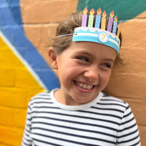 young girl in black and white stripy top smiling and wearing a paper birthday crown with seven candles
