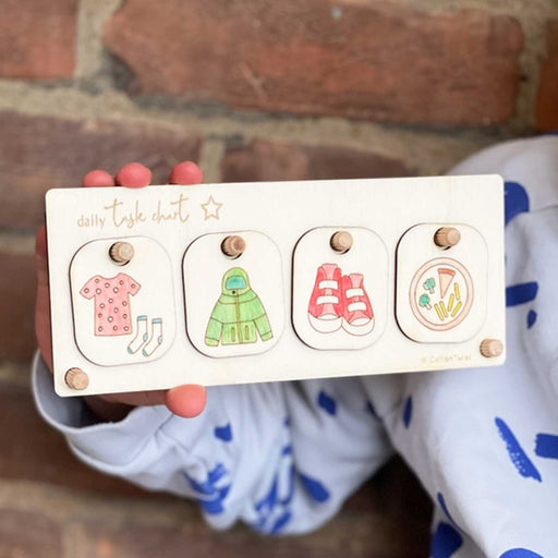 CHILD HOLDING A WOODEN DAILY TASK CHART WITH FOR SEGMENTS SHOWING CLOTHES, A COAT, SHOE AND PLATE OF FOOD