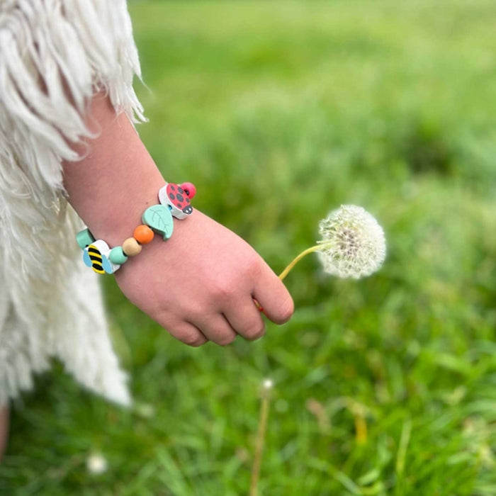 CHILD'S HAND WITH COLOURED WOOODEN BEAD BRACLET HOLDING A DANDELION