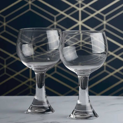 a pair of goblet gin glasses with thick glass stem on a grey table top in front of a navy and gold wall