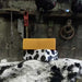 a stack of 2 soaps , one wrapped in cow print paper on a black and white rock in a workshop with tools in the background