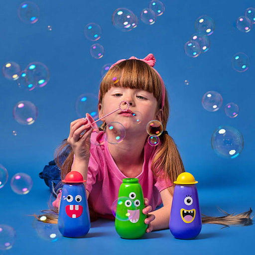 young girl lying on a blue ground blowing bubbles with 3 bubble containers in front of her and bubbles in the air