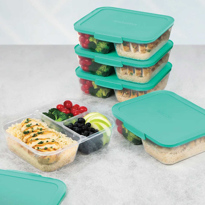 5 clear lunchboxes with green lids on a  grey table. 3 a stacked atop of one another and 2 are sitting side by side in front. One on the left has no lid on it and had food inside its 3 compartments