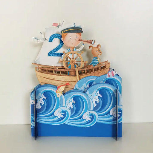 pop up cared showing blue wave ocean with orange fish and brown sailing ship being sailed by a boy in a white hat with dog to his right and a blue sparkly number 2 on ship's sails