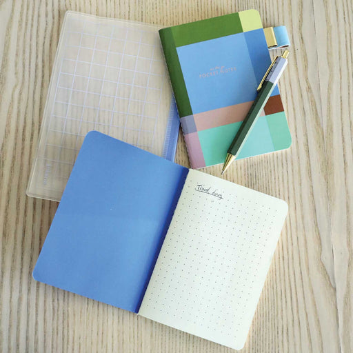 2 notebooks, a green barrel pen and a clear rectangle pencil case on a table top. One of hte notebooks is open to show dotted paper