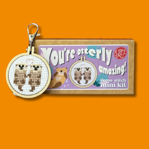 Cross stitch otter keychain with 'You're otterly amazing!' packaging on an orange background
