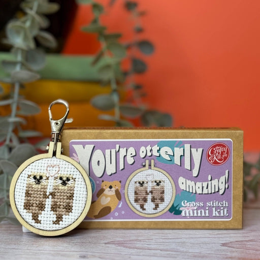 Cross stitch mini kit with completed keychain and packaging on a wooden surface.