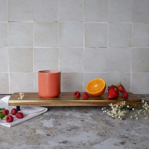 red cu with no handle and pink interior on a small wooden board with raspberries and half an orange