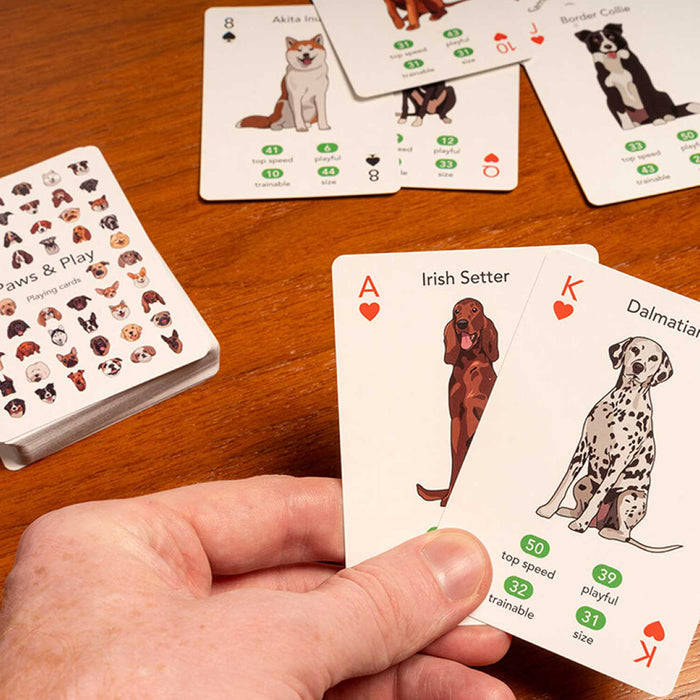 a hand holding 2 cards from Paws & Play Playing Cards featuring dog-themed illustrations