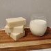 3 stacked bars of white soap beside a glass of milk on a wooden board
