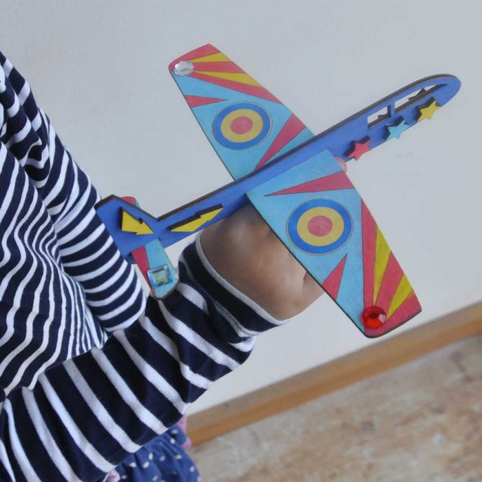 CHILD IN BLACK AND WHITE STRIPED TOP HOLDING A BLUE, RED AND YELLOW WOODEN MODEL AEROPLANE
