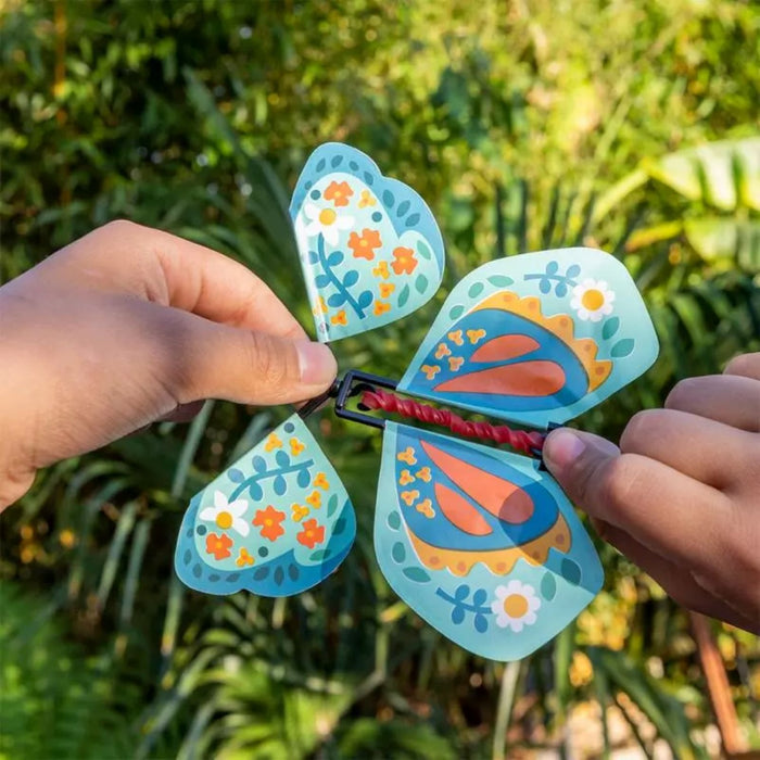 Colorful butterfly-shaped wind spinner held by hands with a green outdoor background