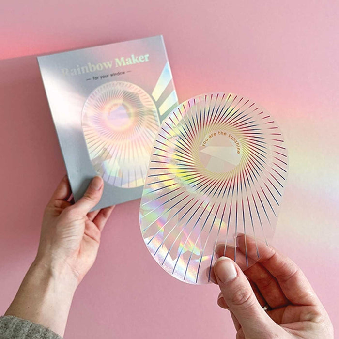 pair of hands hold on irridescent oblong sticker and  sticker package against a pink wall