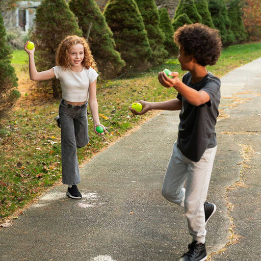 a boy and a girl outside each holding two green water balloon balls, about to throw them at each other