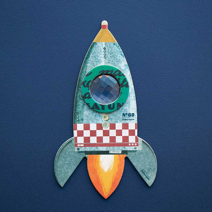 A cardboard rocket with a small kaleidoscopic window at the centre against a blue background.