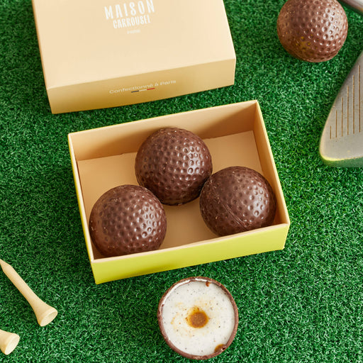 set of 3 chocolate golf balls in box on green grass with golf tees and putter