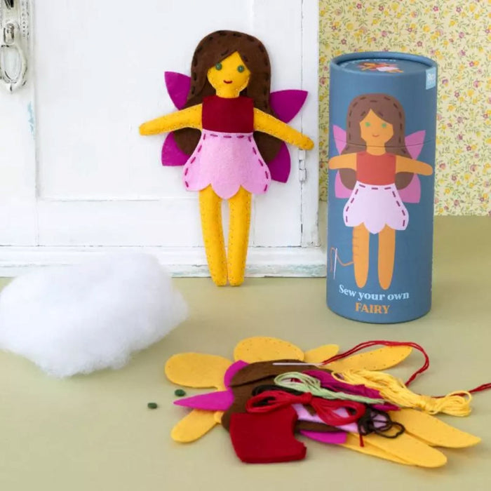 Felt fairy doll kit with materials and a cylindrical container labeled 'Sew your own fairy' on a light surface.
