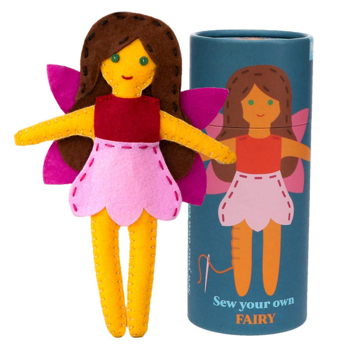 Felt fairy doll with brown hair, red shirt, pink skirt, and yellow arms and legs, next to a blue tube packaging with illustrations and text.