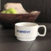 white ceramic cup with Sympathy on the front in blue block capitals with wooden bowl in background holding two green apples