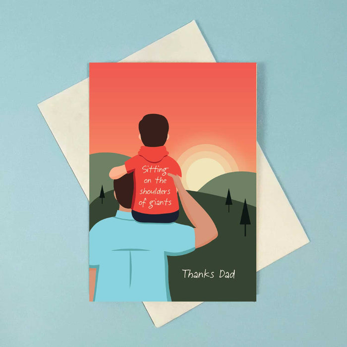 greeting card with young boy sitting on a mans right shoulder with his arm on the man's head. they have their back to us and are watching a sunset over green hills with a red sky 