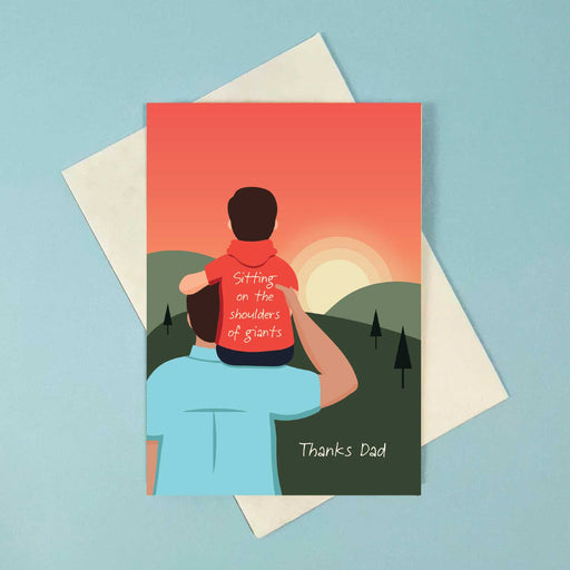 greeting card with young boy sitting on a mans right shoulder with his arm on the man's head. they have their back to us and are watching a sunset over green hills with a red sky 