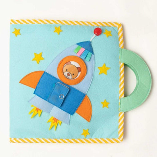 space adventure booklet, blue soft material book with yellow stars and handle and blue spaceship with a smiling teddy's face looking out the window