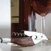 metal bird shaped corkscrew with wooden inlay and bottle and glass of red wine behine