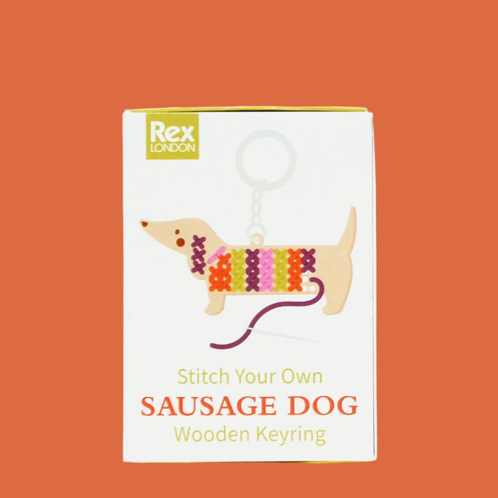Packaging of a 'Stitch Your Own Sausage Dog' wooden keyring kit by Rex London on a white background.