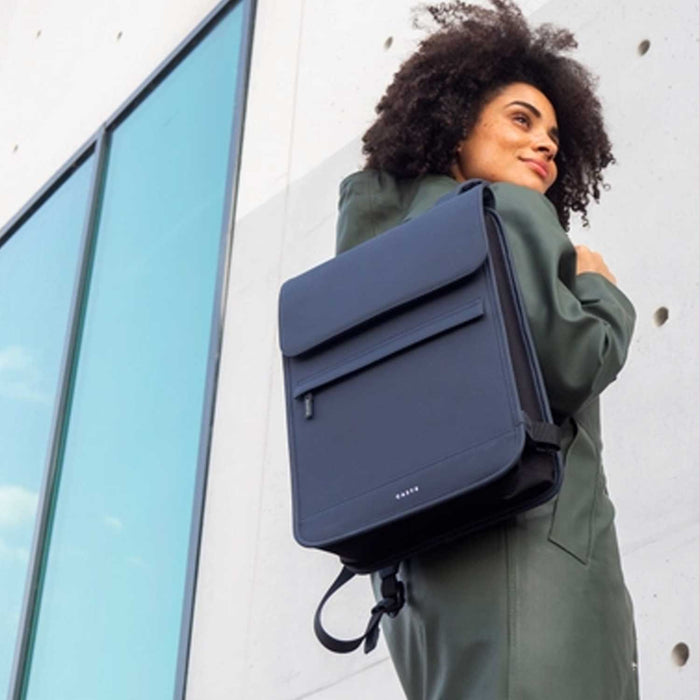 smailing woman in green coat with  blue backpack over her shoulder