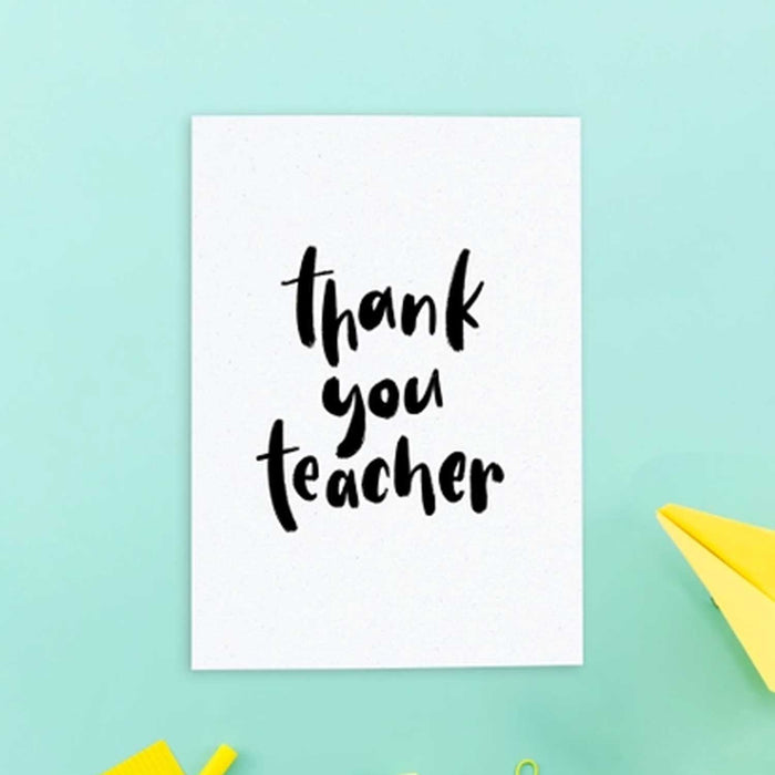 Thank You Teacher greeting card, cream card wbackgroundith black brushstroke style text. Card is against a blue 