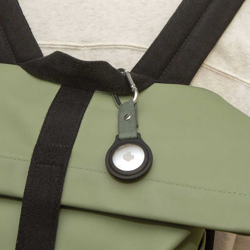 circular apple tracker encased in a green and black clip attached to a black and green backpack
