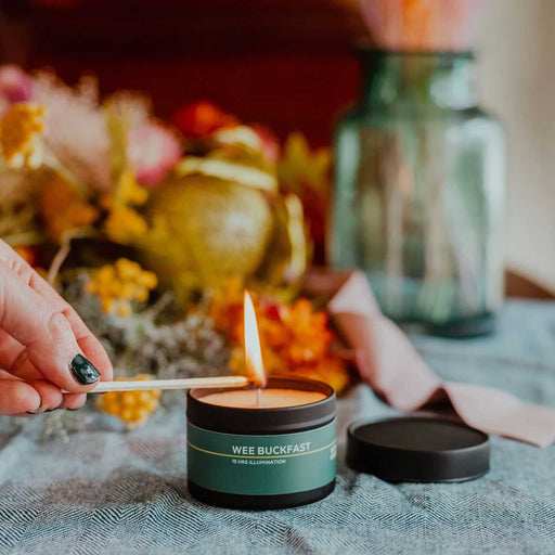 hand lighting a small candle in a tin with green label