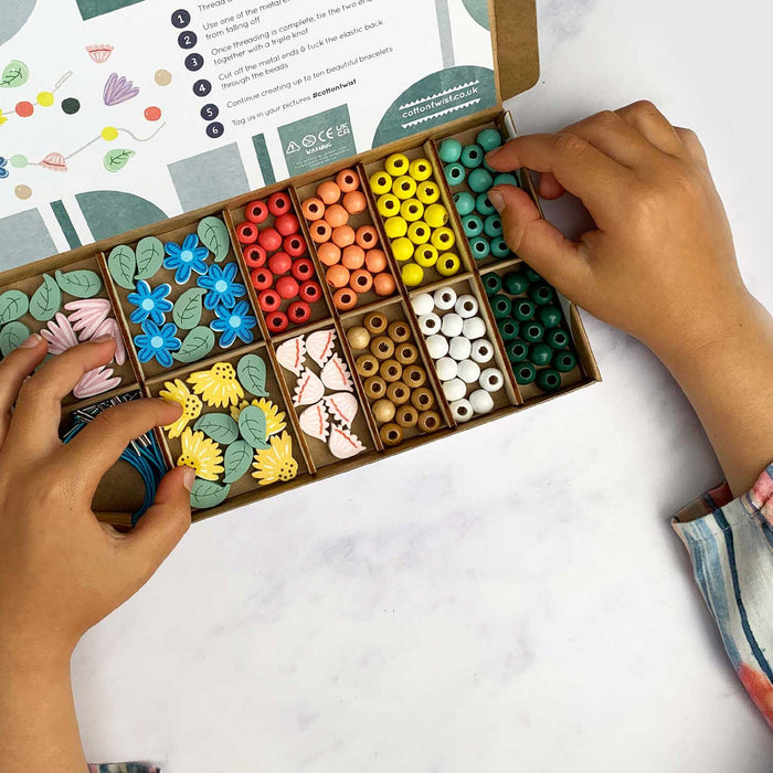 CHILD'S HANDS PICKING A BLUE BEAD FROM A BOX OF BEADS WITH 12 COMPARTMENTS AND A DIFFERENT STYLE OF BEAD IN EACH ONE
