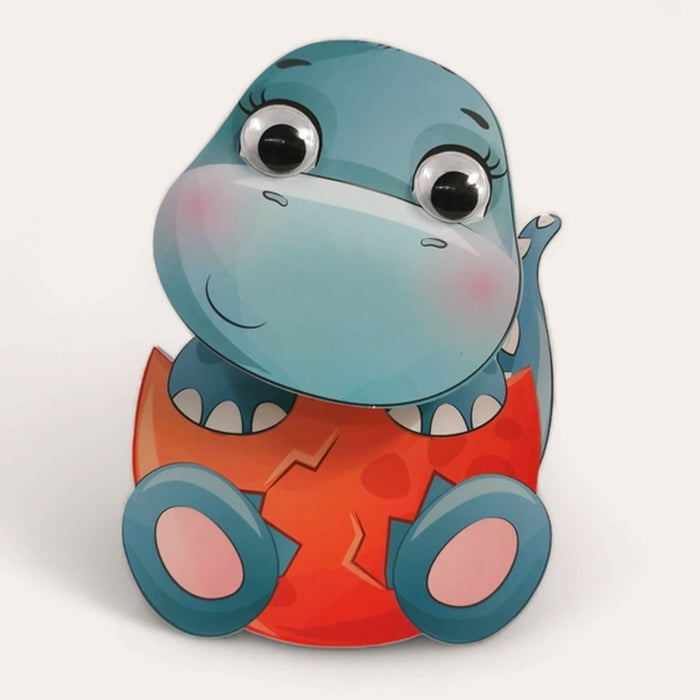 blue dinosaur with google eyes smiling and sitting in a cracked red egg