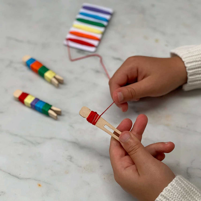 child's hands wrapping red thread around a wooden peg