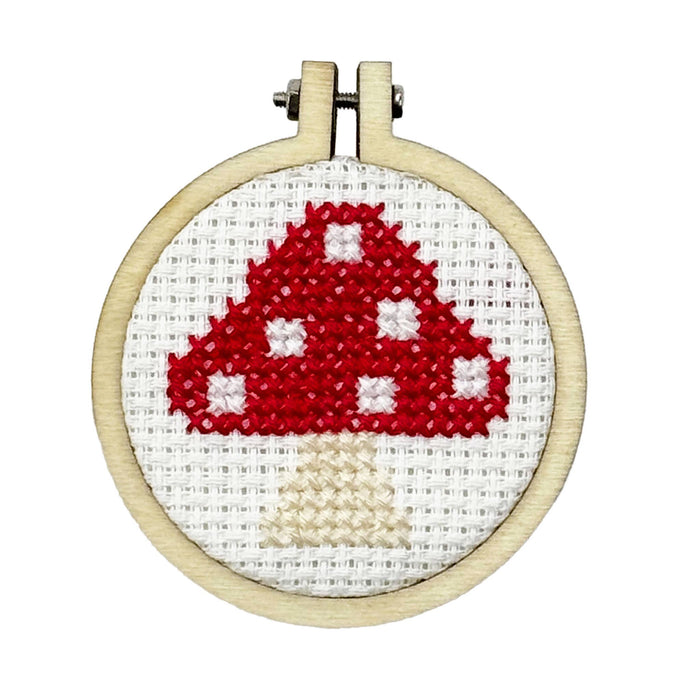 Cross-stitched red mushroom design in a wooden hoop on a white background