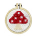 Cross-stitched red mushroom design in a wooden hoop on a white background