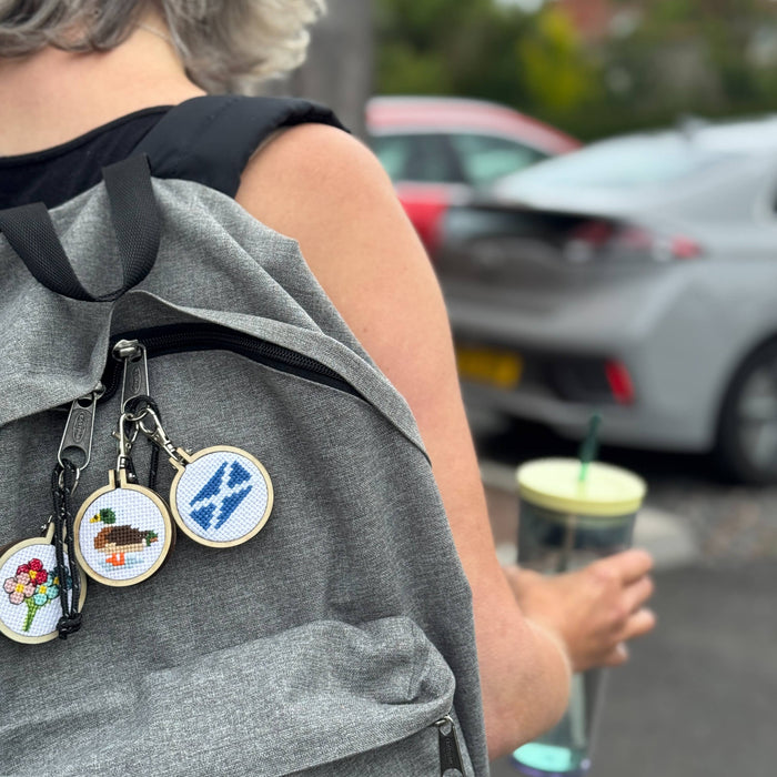 Person with a backpack featuring embroidered charms and a drink in an outdoor setting.