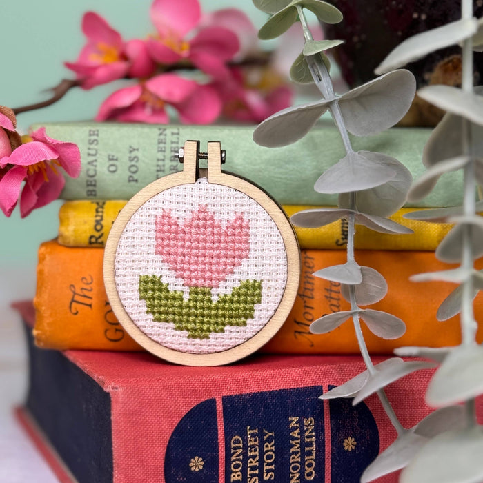 Cross-stitched tulip design on a wooden hoop with books and flowers in the background