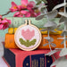 Cross-stitched tulip design on a wooden hoop with books and flowers in the background