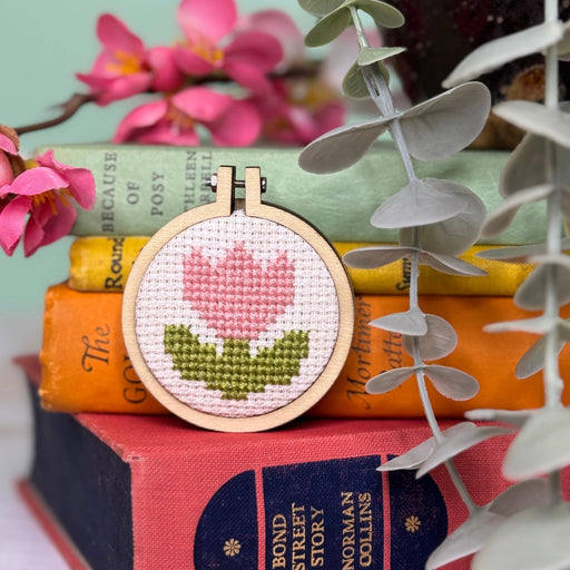 Cross-stitched tulip design on a wooden hoop with books and flowers in the background