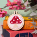 Cross-stitched mushroom design in a wooden hoop on books with flowers and leaves.