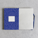 A notebook with a blue patterned cover and blank white pages, laid flat on a light gray textured surface. A blue ribbon bookmark is visible on the right side.