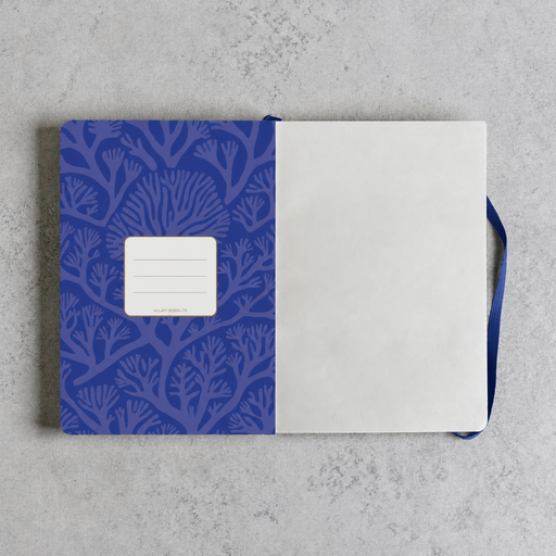 A notebook with a blue patterned cover and blank white pages, laid flat on a light gray textured surface. A blue ribbon bookmark is visible on the right side.
