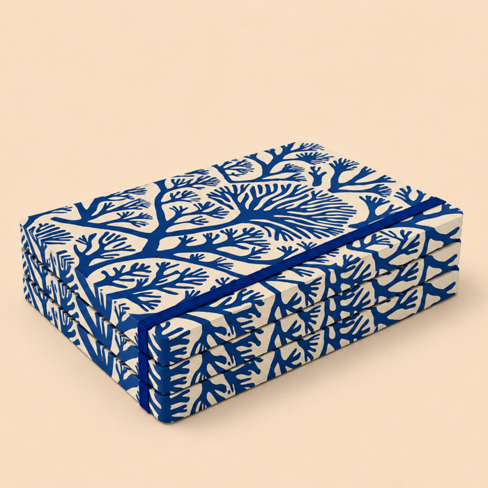 A stack of rectangular boxes wrapped in cream fabric printed with a bold blue coral or branch-like pattern, tied with a matching blue ribbon, on a plain beige background.